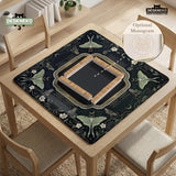 A dark floral mahjong mat with a scalloped edge, moth and flower artwork, and an American Mahjong rules layout on a dark background.