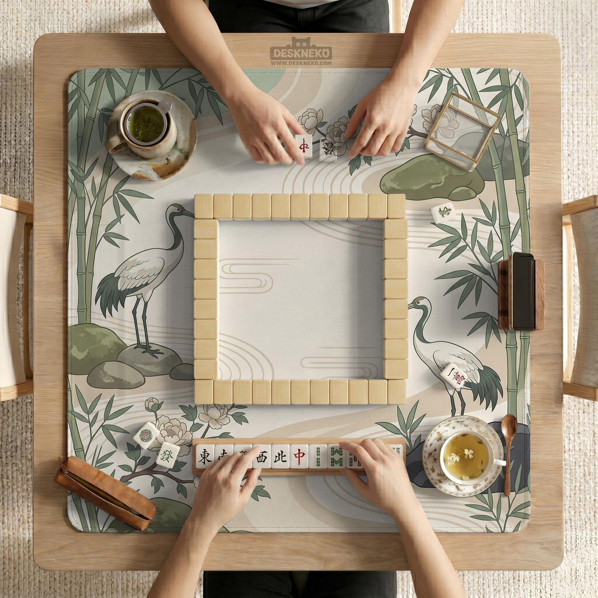 Square mahjong mat with a cream background, sage green cranes, bamboo leaves, peony branches, stones, and thin linework.