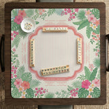Coral tropical floral mahjong mat with hibiscus flowers, palm leaves, cream sections, and a scalloped edge.