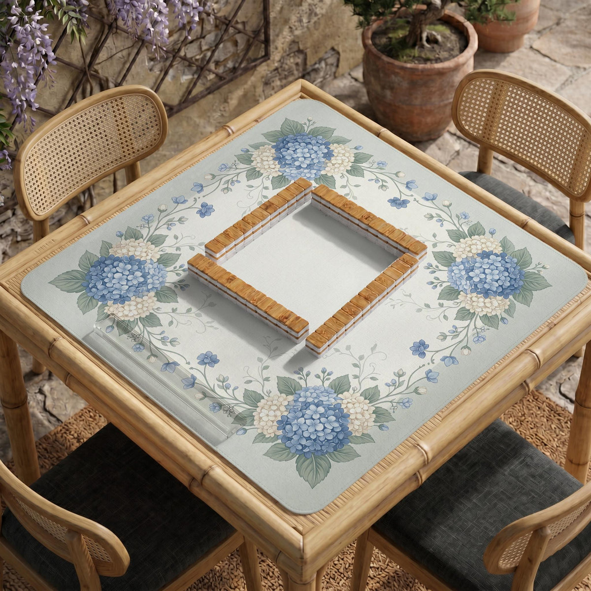 A square blue mahjong mat with hydrangea flowers, cream blossoms, sage leaves, and vines around a plain center play area. The edge is scalloped.