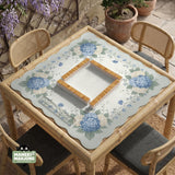 A square blue mahjong mat with hydrangea flowers, cream blossoms, sage leaves, and vines around a plain center play area. The edge is scalloped.