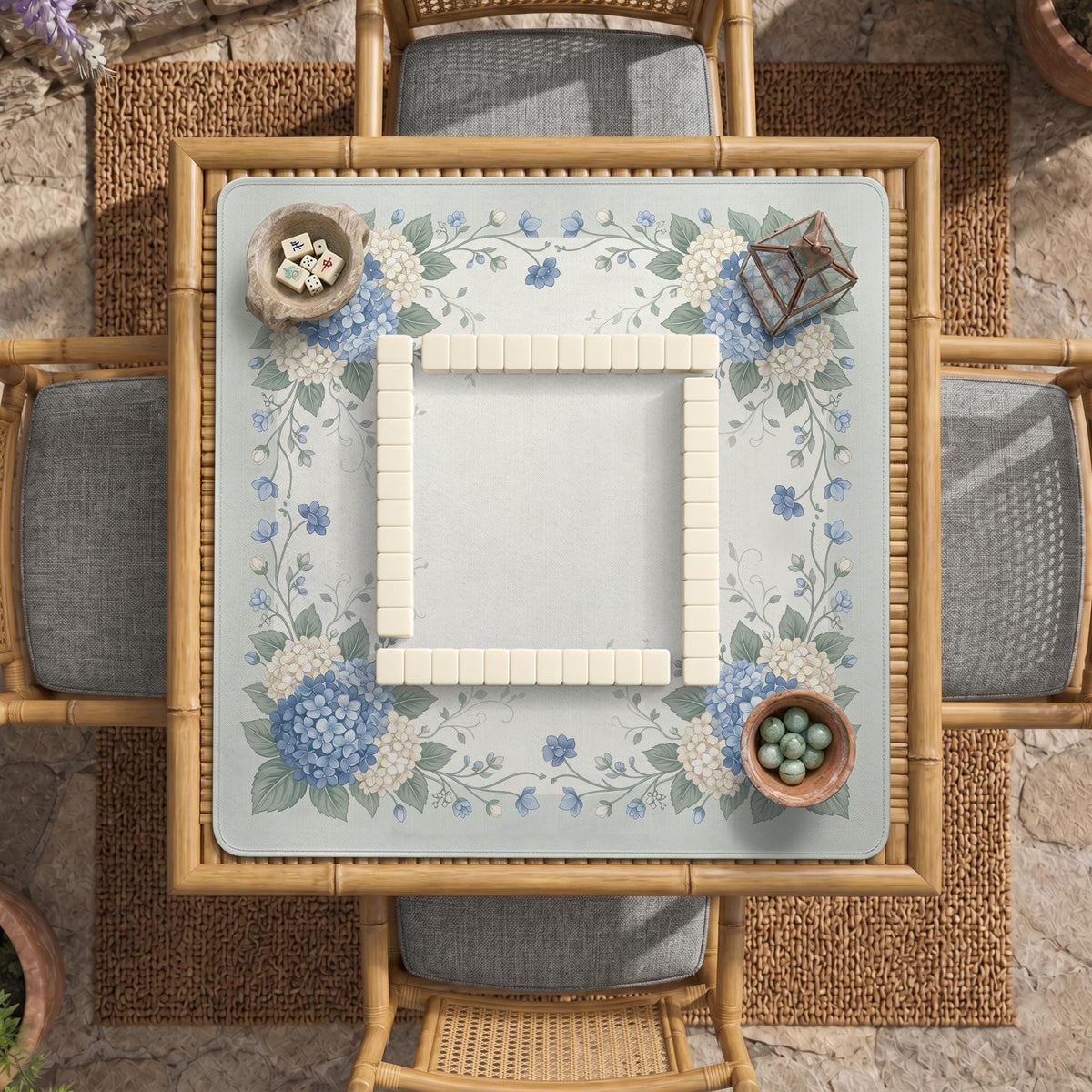 A square blue mahjong mat with hydrangea flowers, cream blossoms, sage leaves, and vines around a plain center play area. The edge is scalloped.