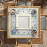 A square blue mahjong mat with hydrangea flowers, cream blossoms, sage leaves, and vines around a plain center play area. The edge is scalloped.