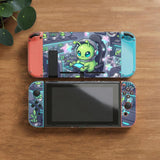 A Switch carrying case design with a cute green alien at a gaming desk, glowing cyan lights, and pastel stars on a dark background.