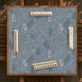 Blue mahjong mat with a dusty linen-look background and small leafy botanical stems in a floral pattern.