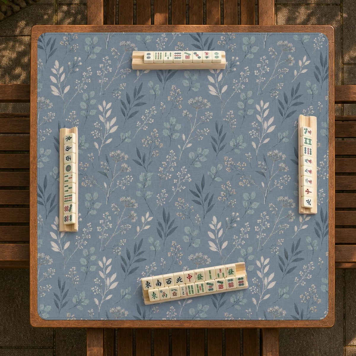 Blue mahjong mat with a botanical floral pattern, pale leaves, and delicate stems on a dusty blue background.