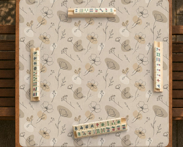 Neutral floral mahjong mat with delicate botanical line art and a scalloped edge on a cream background.