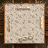 Neutral floral mahjong mat with delicate botanical line art and a scalloped edge on a cream background.