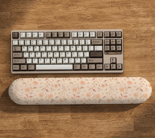 Blush pink floral mouse pad with wrist rest options, shown with peach blossoms, muted leaves, and a warm cream background.
