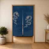 Straight-on view of the two-panel indigo dragon noren in a wooden doorway with a woven rug below.