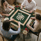 Green mahjong mat with red cardinals, holly berries, cream poinsettias, and gold seasonal details around a printed Charleston guide.