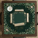 Square mahjong mat with a forest green botanical design, fern leaves, small cream flowers, and a printed Charleston guide around the center area.