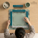 American mahjong mat with a sage-green pond scene, blue-grey herons, water lilies, reeds, and printed play-direction reminders around the edge.