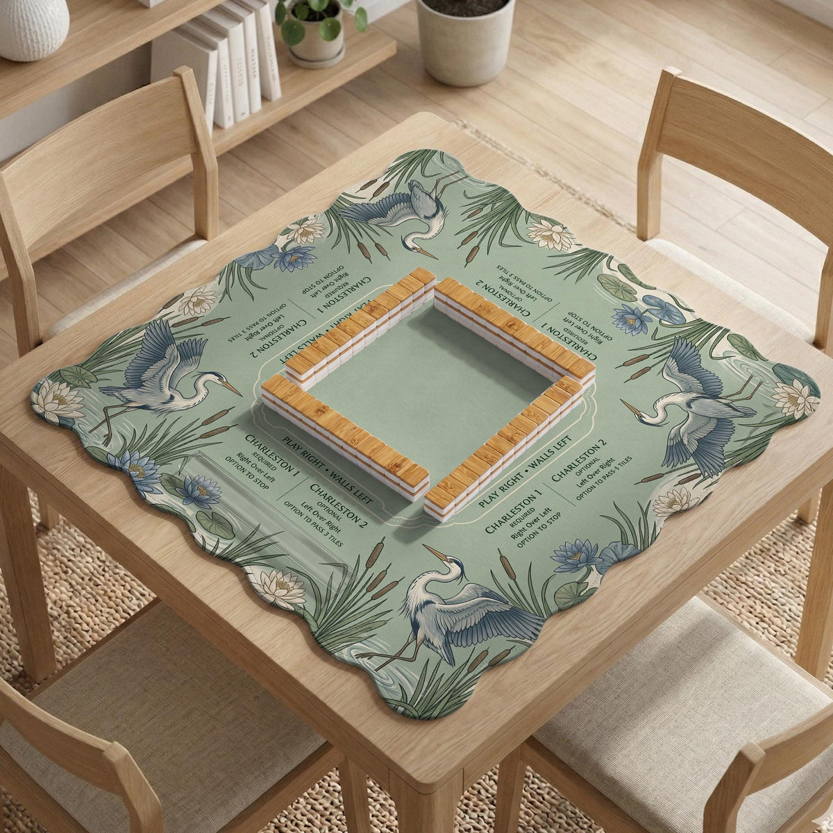 American mahjong mat with a sage-green pond scene, blue-grey herons, water lilies, reeds, and printed play-direction reminders around the edge.