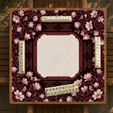Cream American mahjong mat with a burgundy border of pale pink magnolia blossoms and printed play-direction and passing reminders.