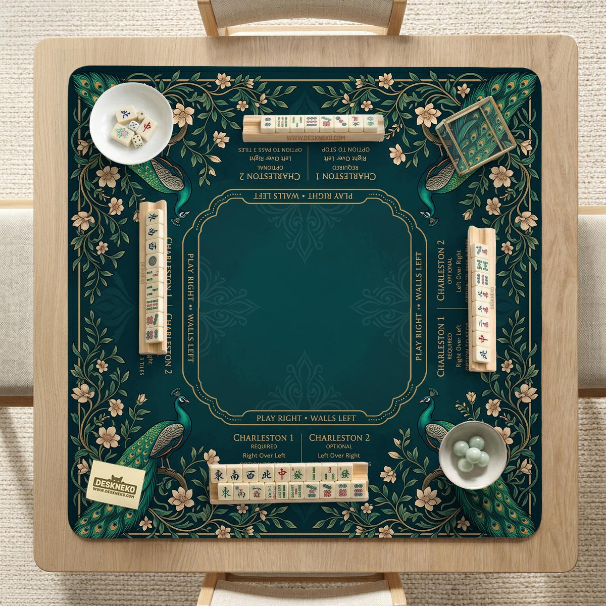 American mahjong mat with a deep teal-green background, peacocks, small cream flowers, leafy branches, and printed play-direction and Charleston reminders.