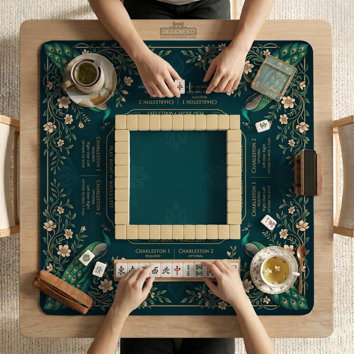 American mahjong mat with a deep teal-green background, peacocks, small cream flowers, leafy branches, and printed play-direction and Charleston reminders.