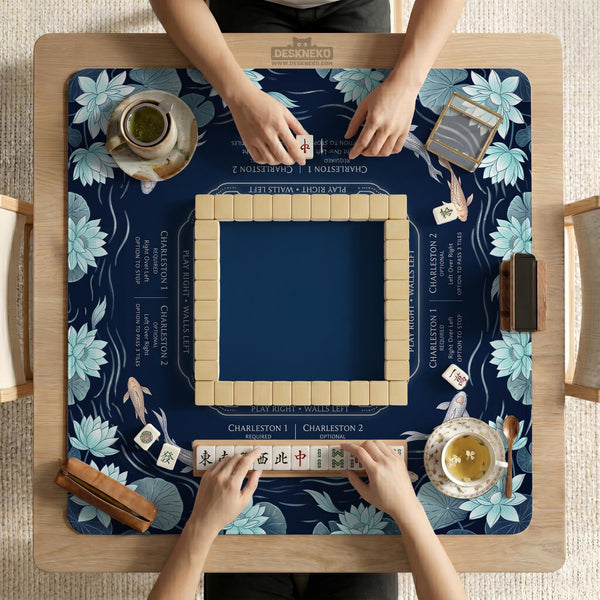 American mahjong mat with a navy-blue pond design, pale aqua lotus flowers, flowing water lines, koi fish, and printed play-direction and Charleston passing reminders.