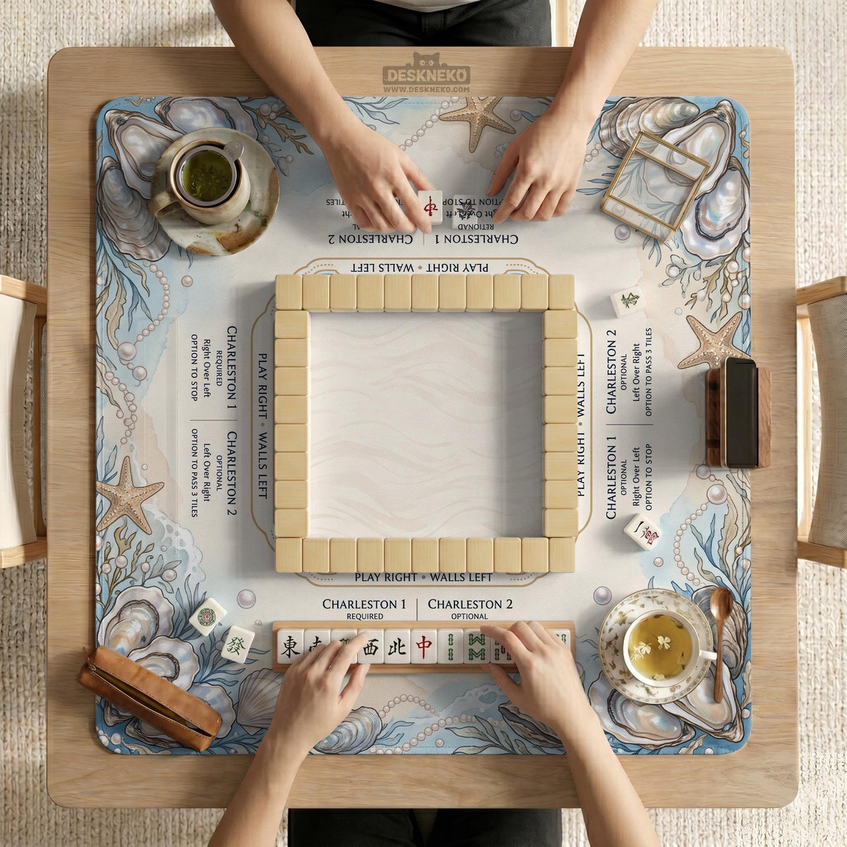 American mahjong mat with a cream center and a coastal border showing oyster shells, scallop shells, starfish, pearl strands, and pale blue sea plants.