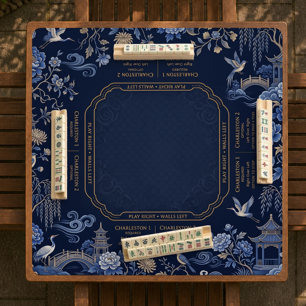 Navy mahjong mat with cranes, garden birds, pagodas, and blue and cream floral designs around a framed playing area with a printed Charleston guide.