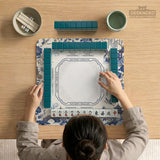 Square ivory mahjong mat with blue cranes, pagodas, flowers, and a blue border around the playing area.