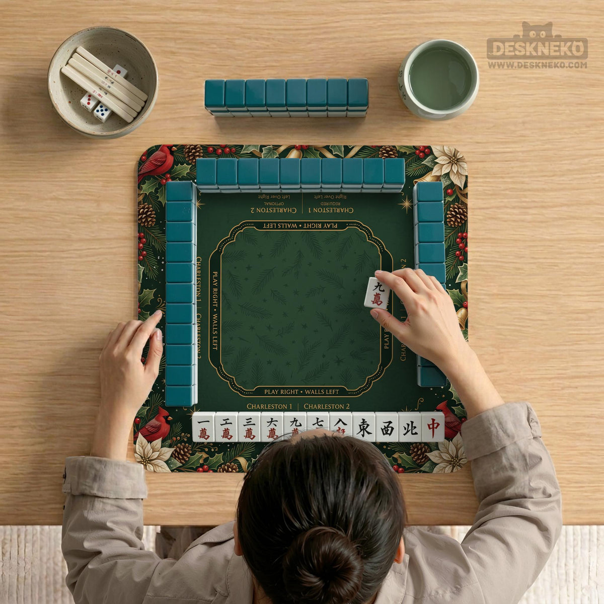 Green mahjong mat with red cardinals, holly berries, cream poinsettias, and gold seasonal details around a printed Charleston guide.