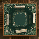 Square mahjong mat with a forest green botanical design, fern leaves, small cream flowers, and a printed Charleston guide around the center area.