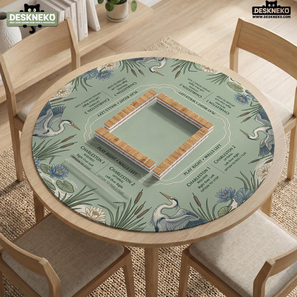 American mahjong mat with a sage-green pond scene, blue-grey herons, water lilies, reeds, and printed play-direction reminders around the edge.