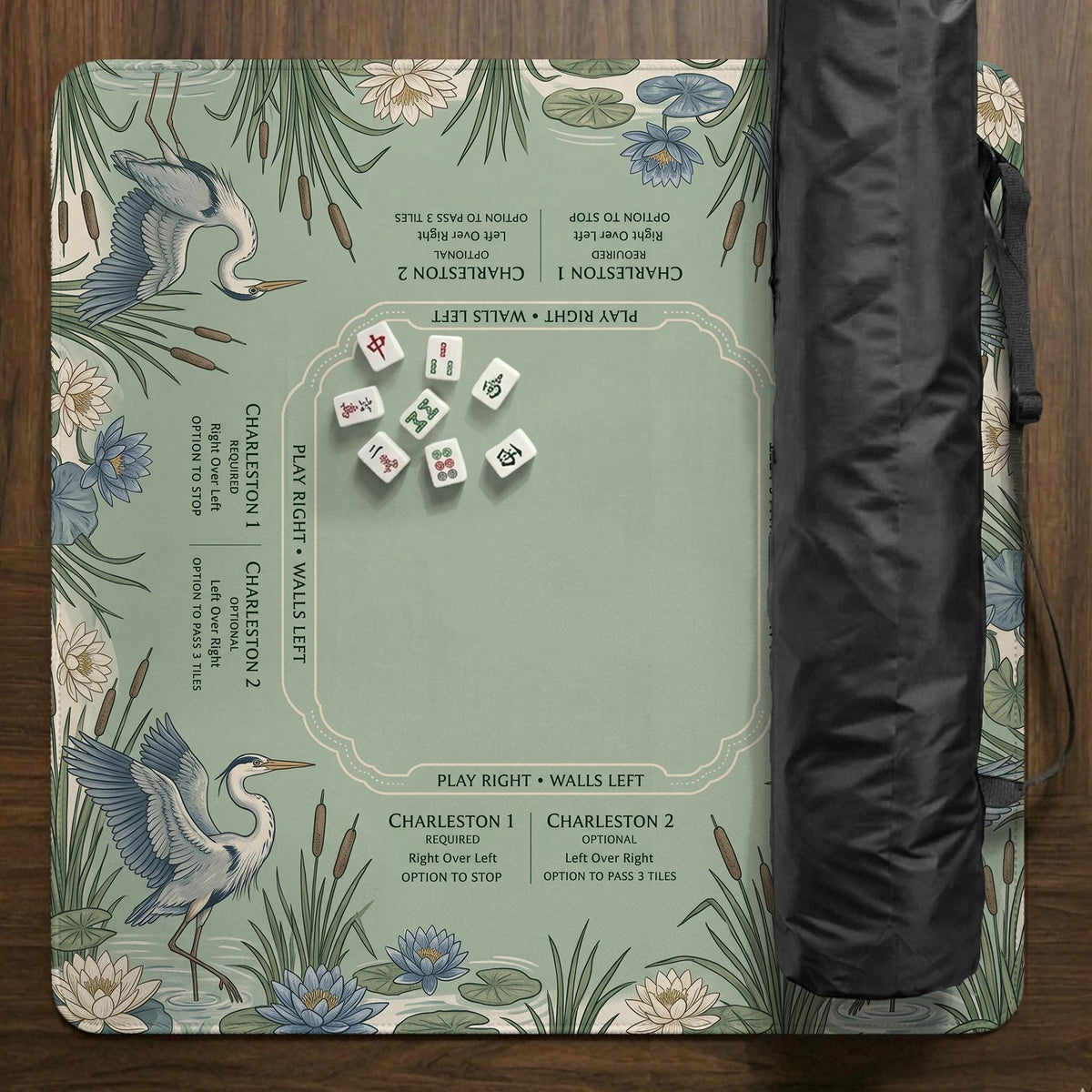 American mahjong mat with a sage-green pond scene, blue-grey herons, water lilies, reeds, and printed play-direction reminders around the edge.