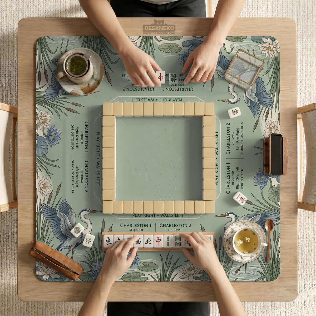 American mahjong mat with a sage-green pond scene, blue-grey herons, water lilies, reeds, and printed play-direction reminders around the edge.