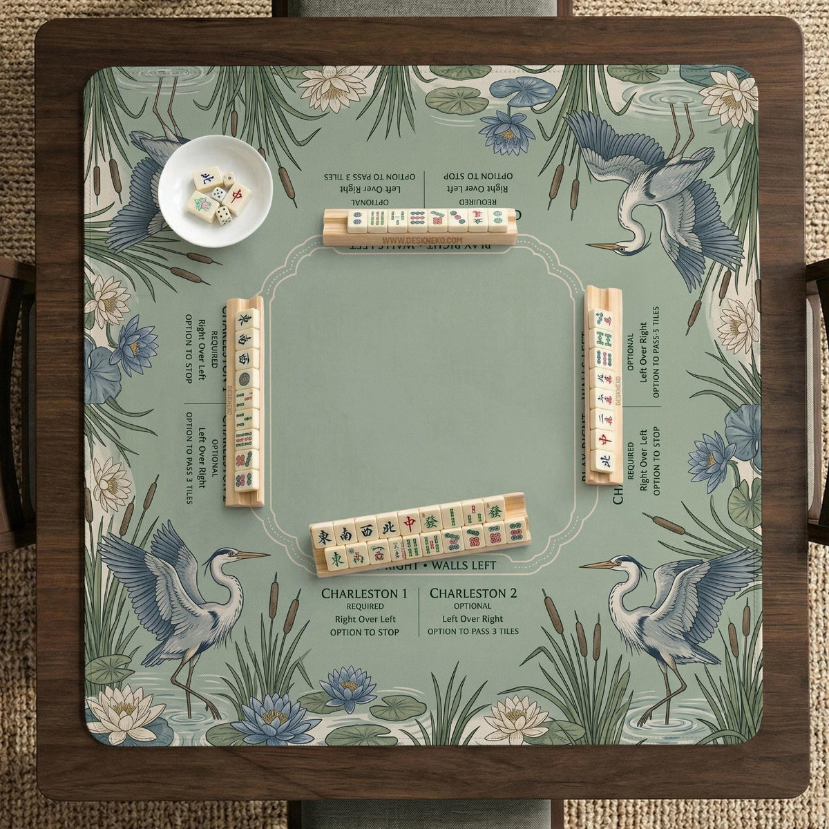 American mahjong mat with a sage-green pond scene, blue-grey herons, water lilies, reeds, and printed play-direction reminders around the edge.