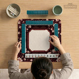 Cream American mahjong mat with a burgundy border of pale pink magnolia blossoms and printed play-direction and passing reminders.