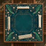 American mahjong mat with a deep teal-green background, peacocks, small cream flowers, leafy branches, and printed play-direction and Charleston reminders.