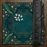 American mahjong mat with a deep teal-green background, peacocks, small cream flowers, leafy branches, and printed play-direction and Charleston reminders.