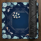 American mahjong mat with a navy-blue pond design, pale aqua lotus flowers, flowing water lines, koi fish, and printed play-direction and Charleston passing reminders.