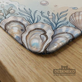 American mahjong mat with a cream center and a coastal border showing oyster shells, scallop shells, starfish, pearl strands, and pale blue sea plants.